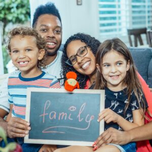 Home Smiling family of four indoors holding a blackboard with 'family' written on it.